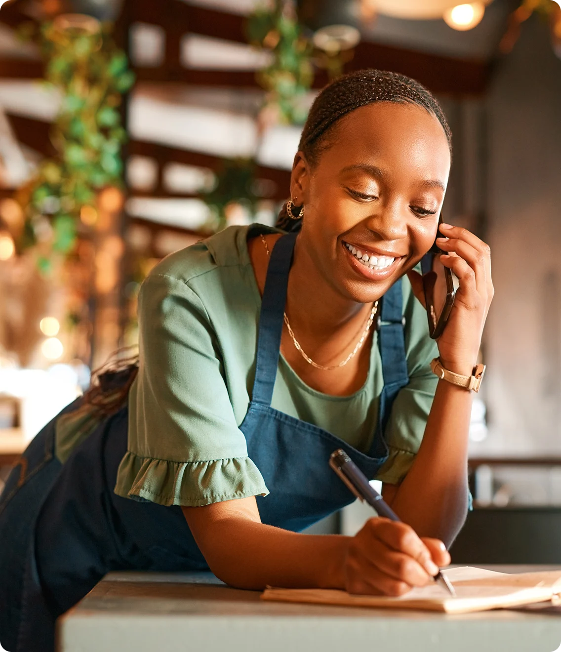 Smiling restaurant staff member in apron talking on phone while taking takeout order