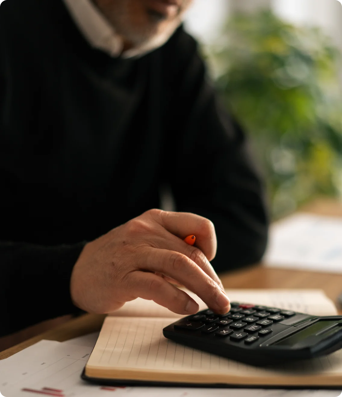 Close-up of a hand using a calculator over a notebook and paperwork.