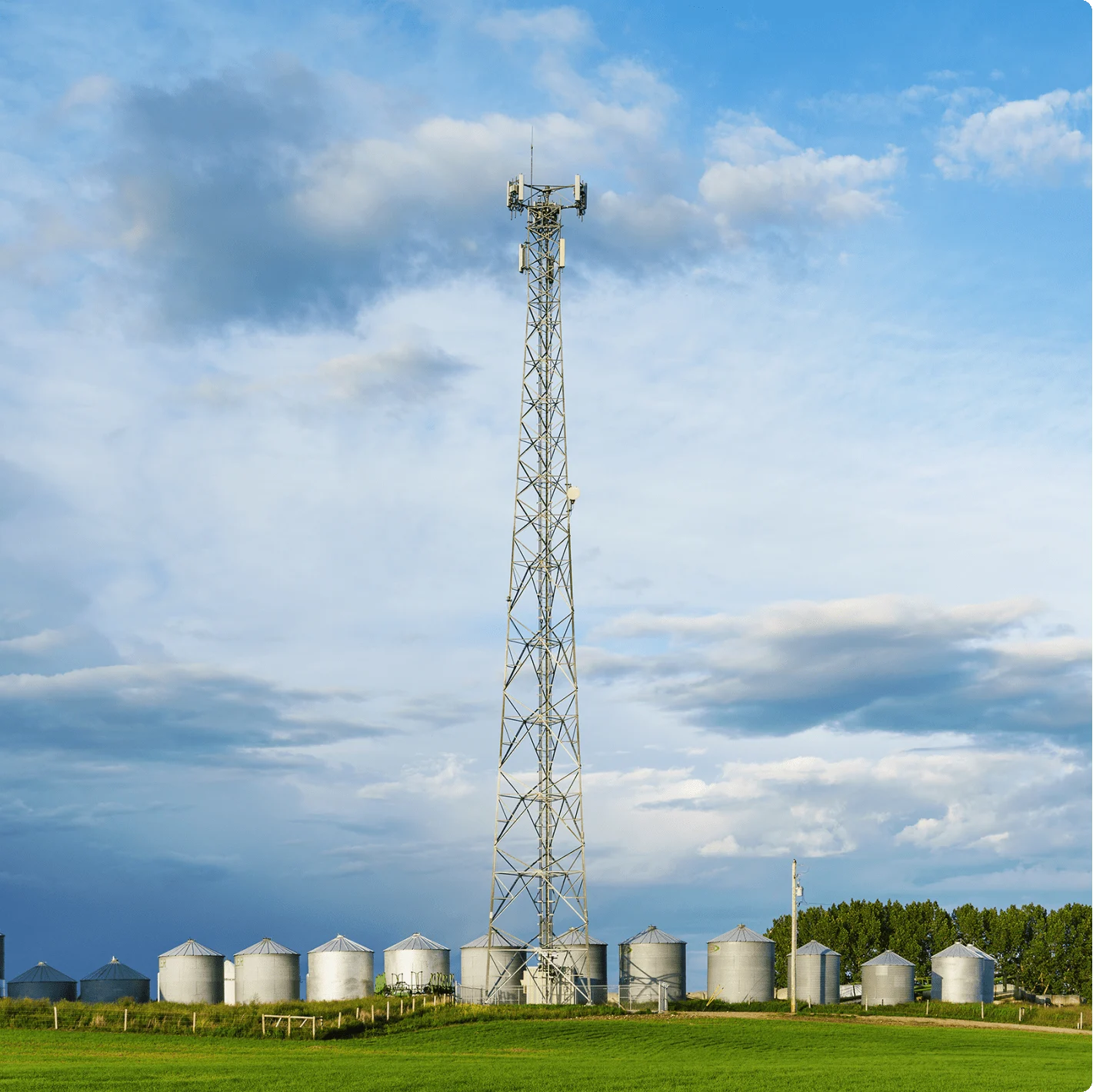 A cellular tower in a field with a line of grain storage bins at its base