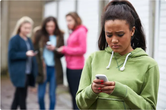 Jeune regardant un téléphone intelligent avec trois autres jeunes en arrière-plan.