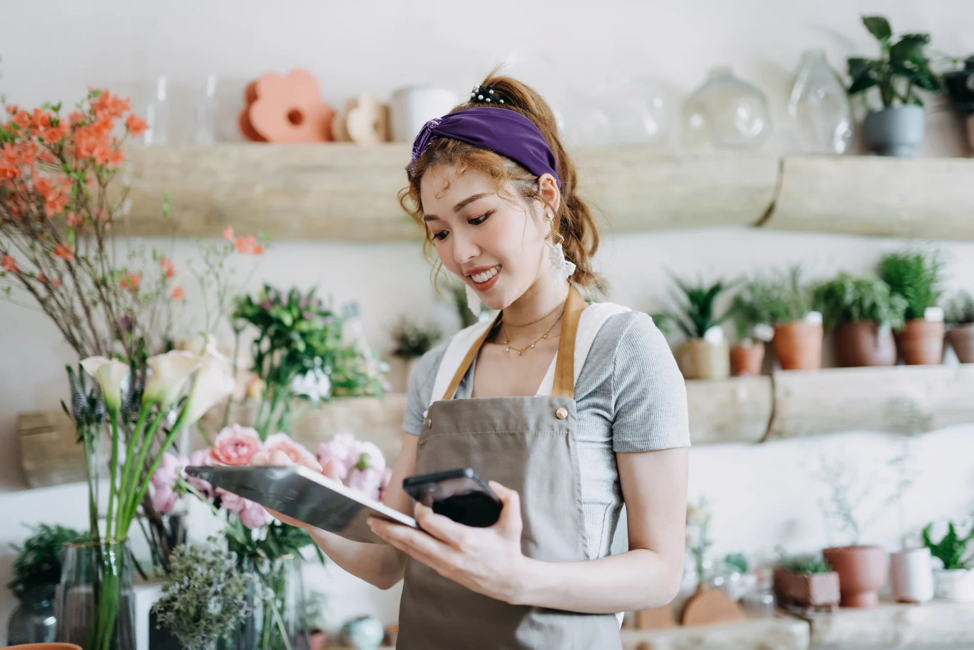 A person using a tablet and mobile device in a flower shop.