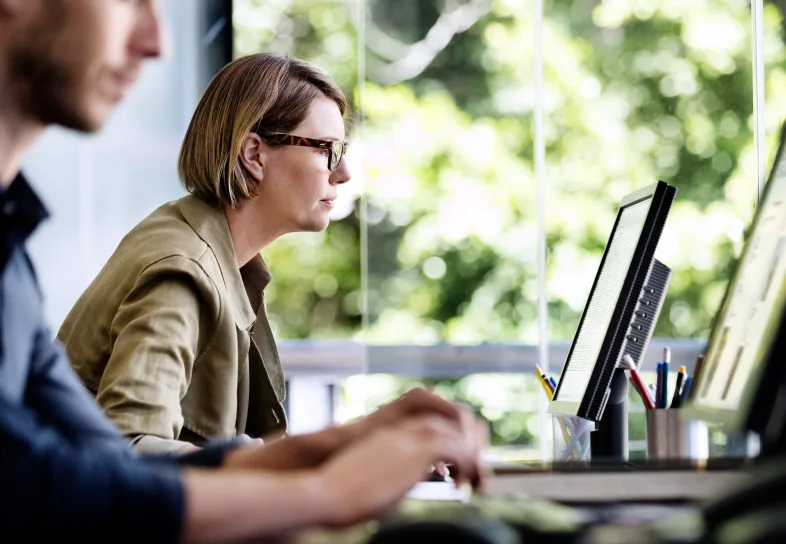 Two people working in an office on their desktop computers.