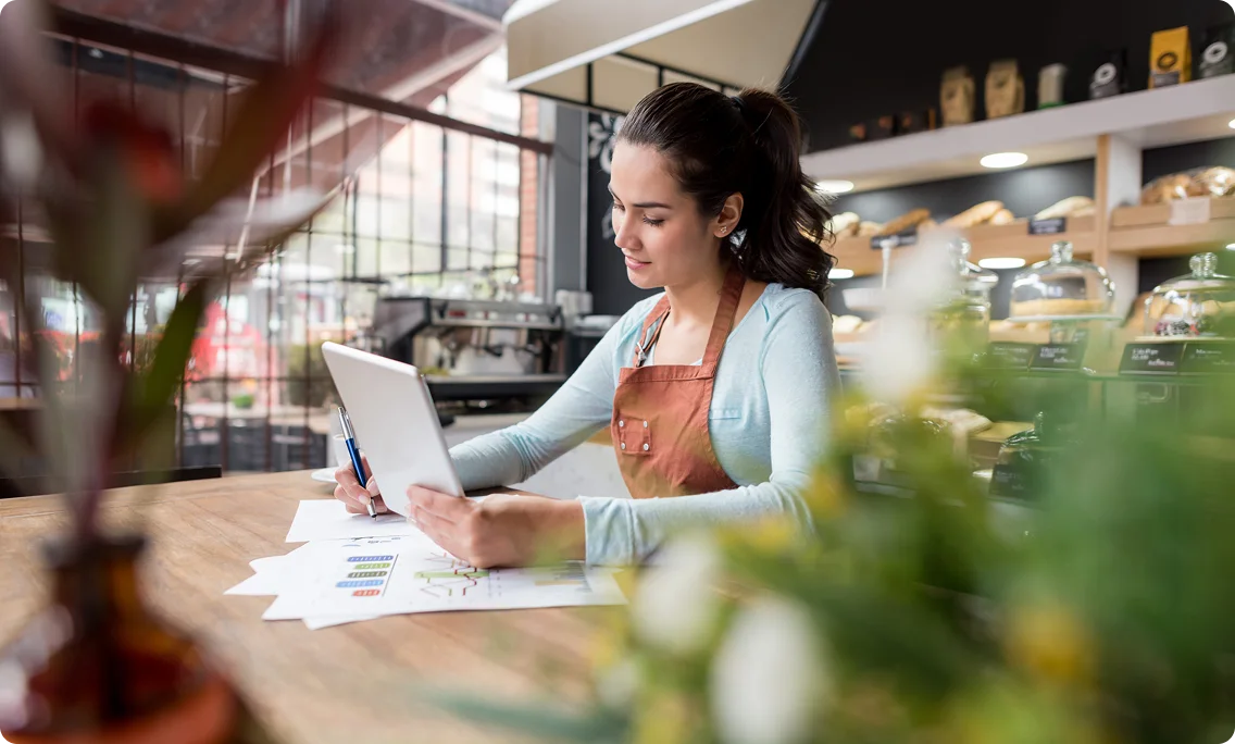 Small business owner reviewing documents and working on a laptop in cafe.