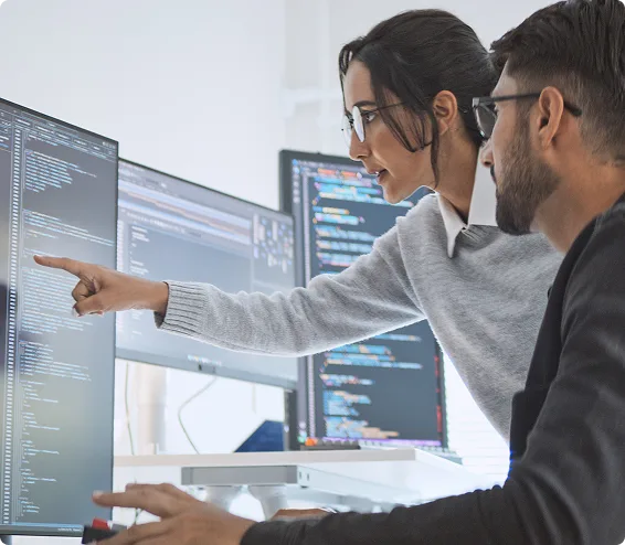 Technology professionals reviewing code and data on multiple monitors.