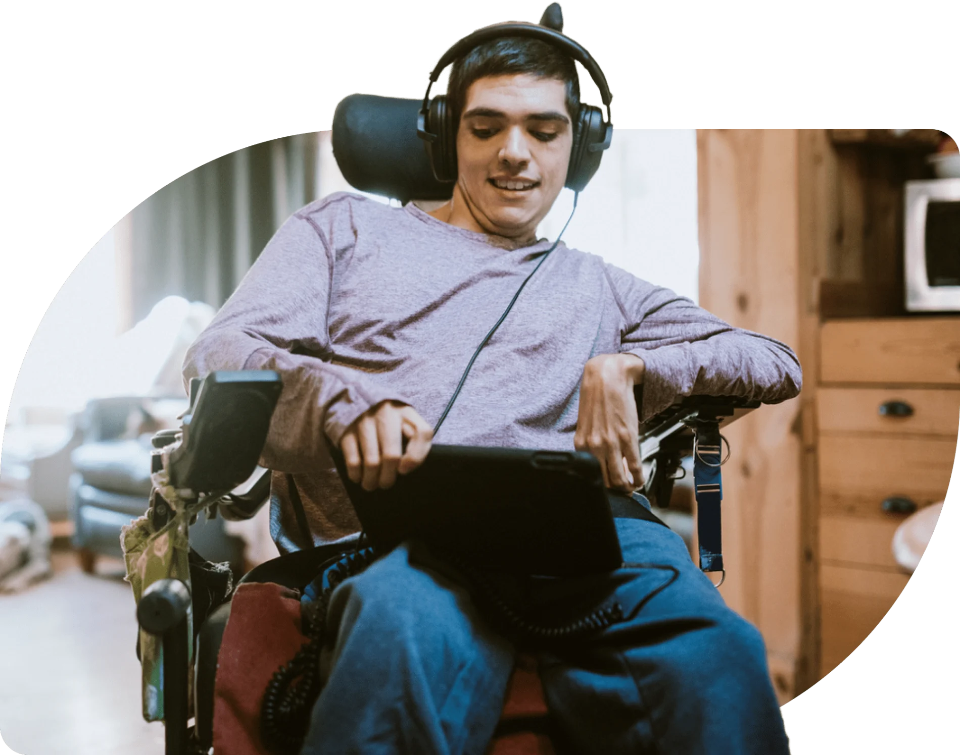 A young man in a wheelchair laughing as he observes a tablet screen
