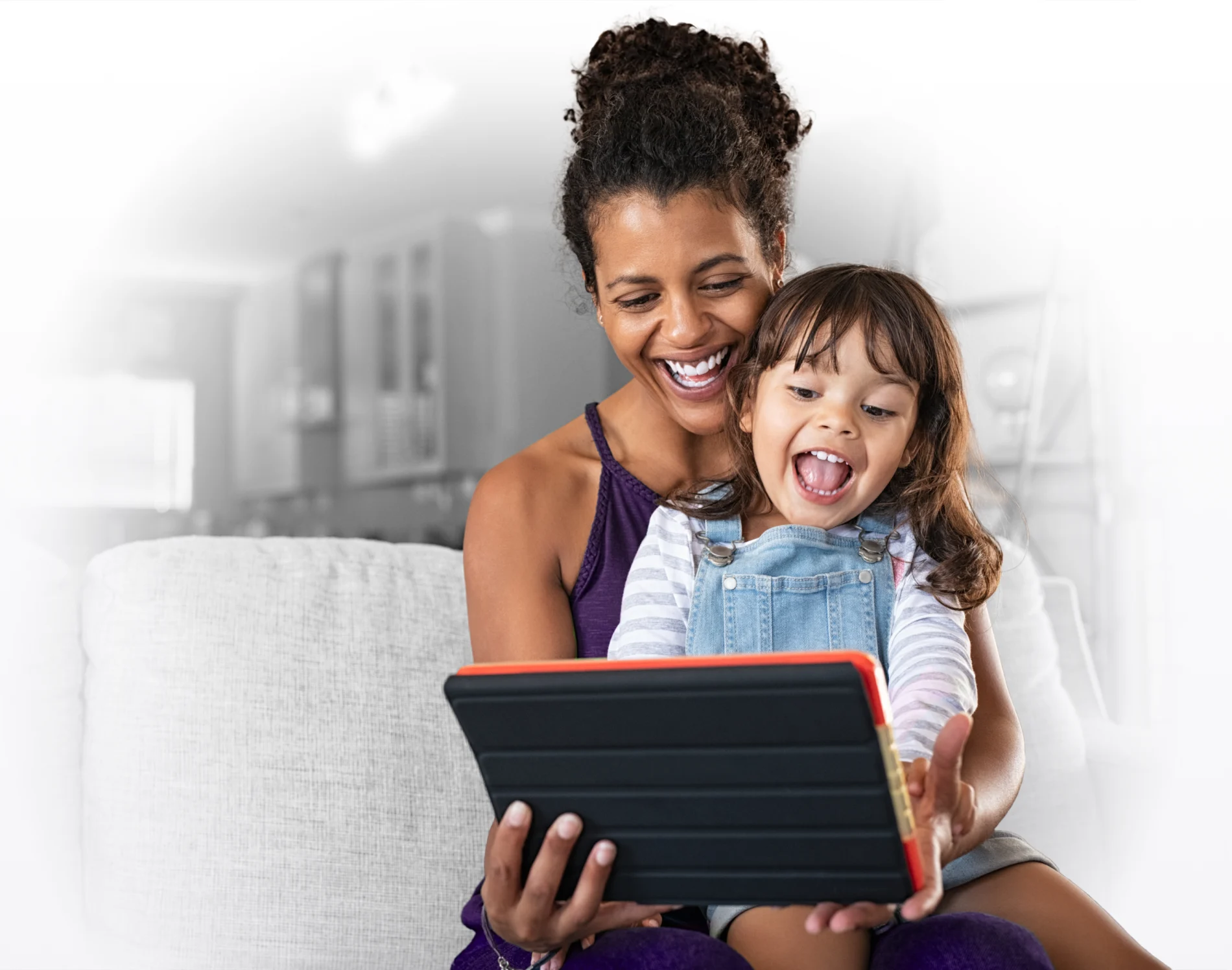 A woman and young child smiling while viewing a tablet