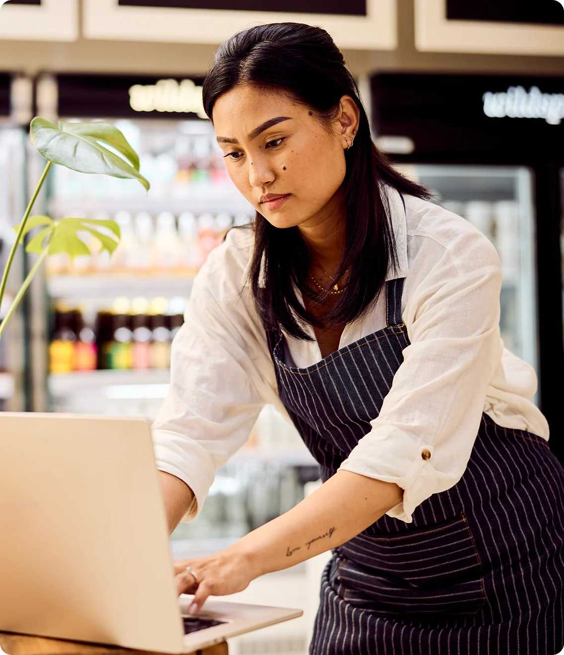 Shop owner in an apron works on a laptop at the counter.