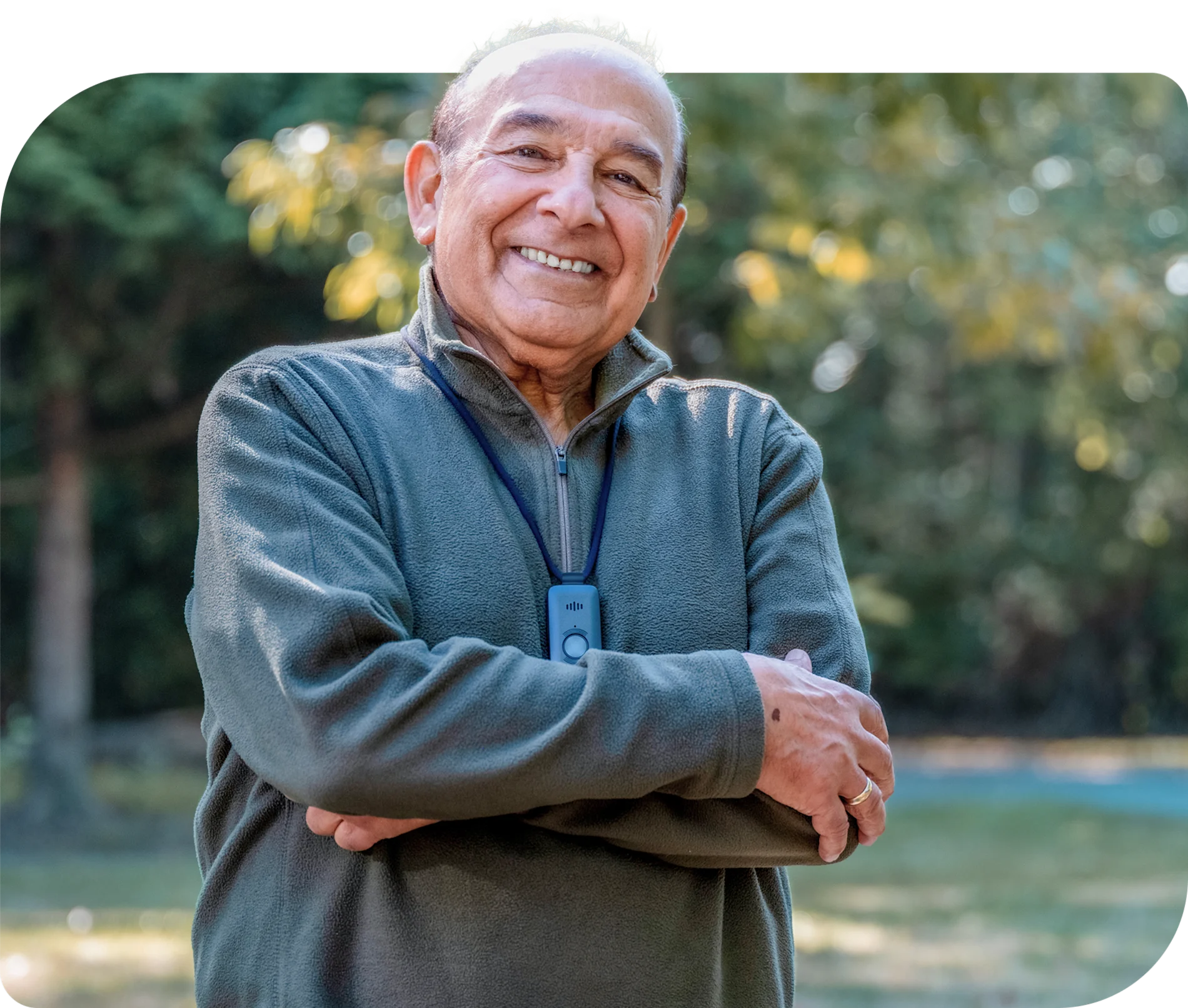 A older man smiling in a park wearing a TELUS Health Medical Alert Pendant
