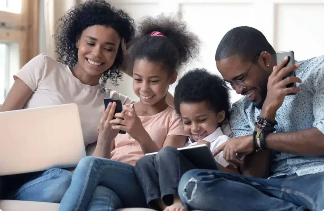 A family seated together interacts with each other and a variety of electronic devices.