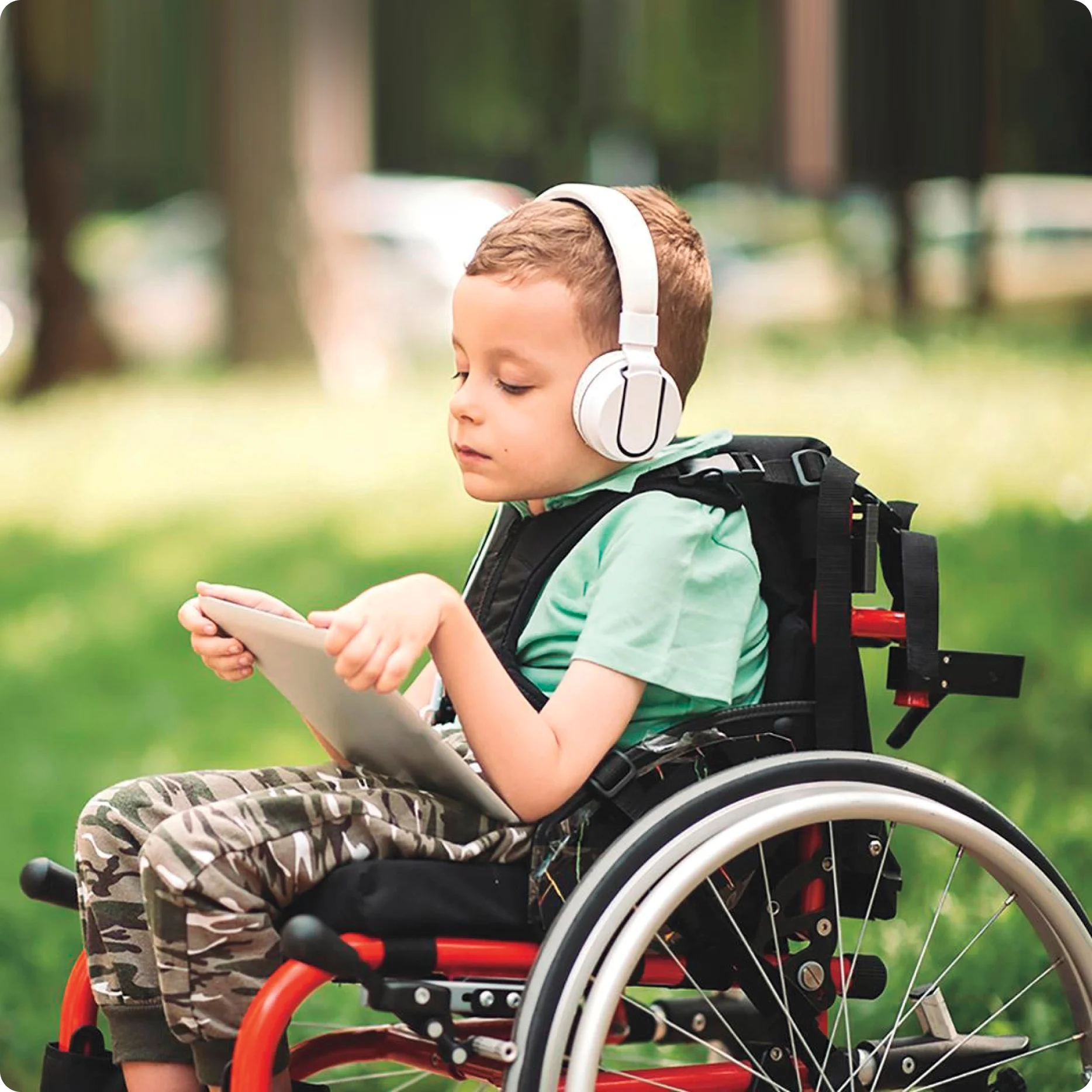 A child in a wheelchair reading a tablet while wearing headphones