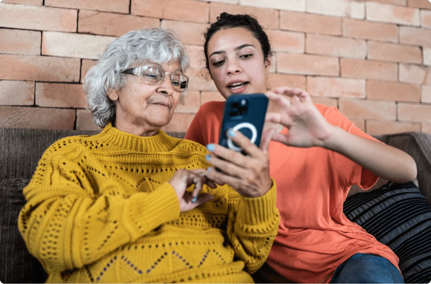 A young person and a senior sitting together and interacting with a smartphone.