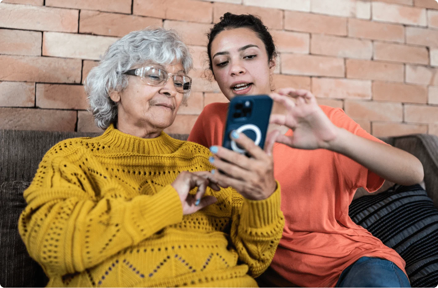 Une jeune et une personne âgée sont assises ensemble et utilisent un téléphone intelligent.