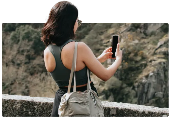 A woman standing outdoors with her back to the camera viewing a smartphone.