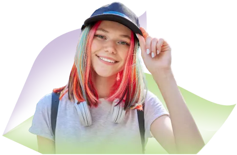A teenager with brightly coloured hair wearing a cap and smiling at the camera.