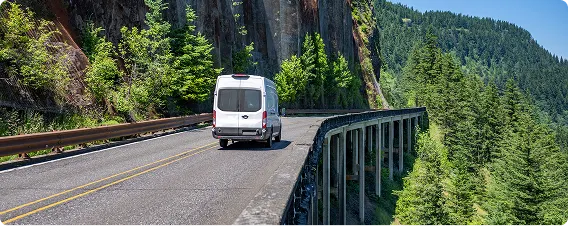 White delivery van driving on coastal mountain road.
