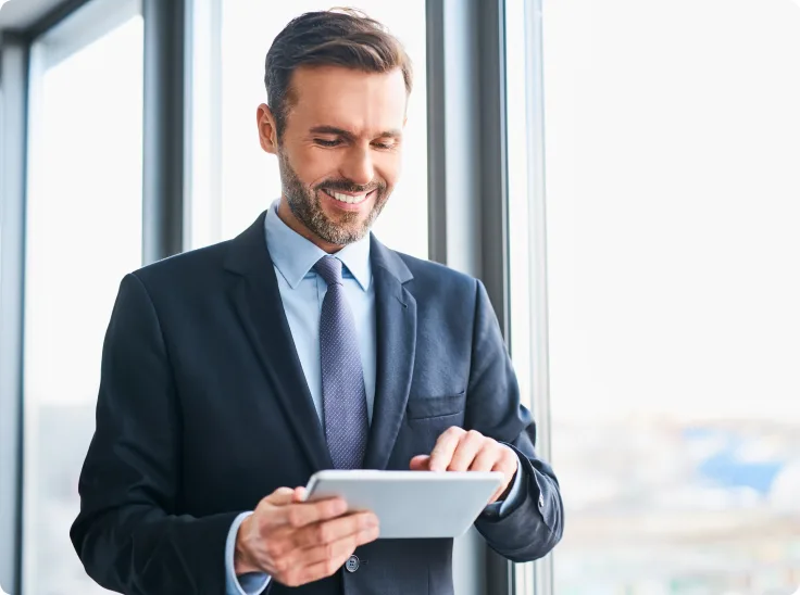 Man standing next to a window while using a digital tablet.