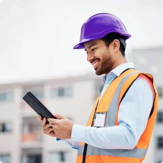 A man in a construction vest and hat looking at his tablet