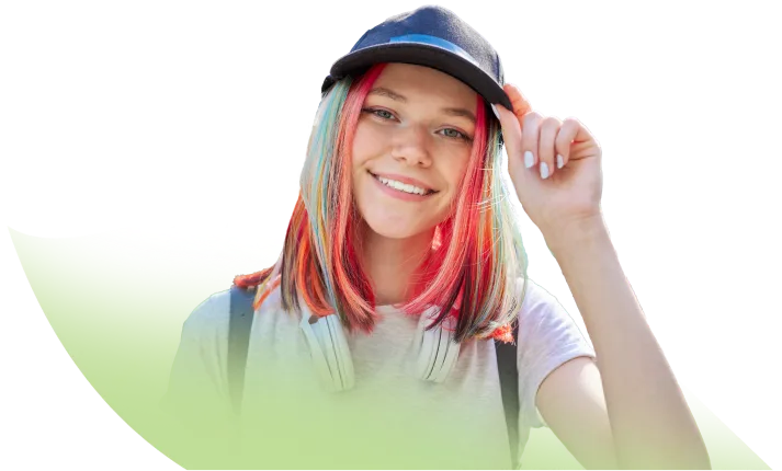 A teenager with brightly coloured hair wearing a cap and smiling at the camera.