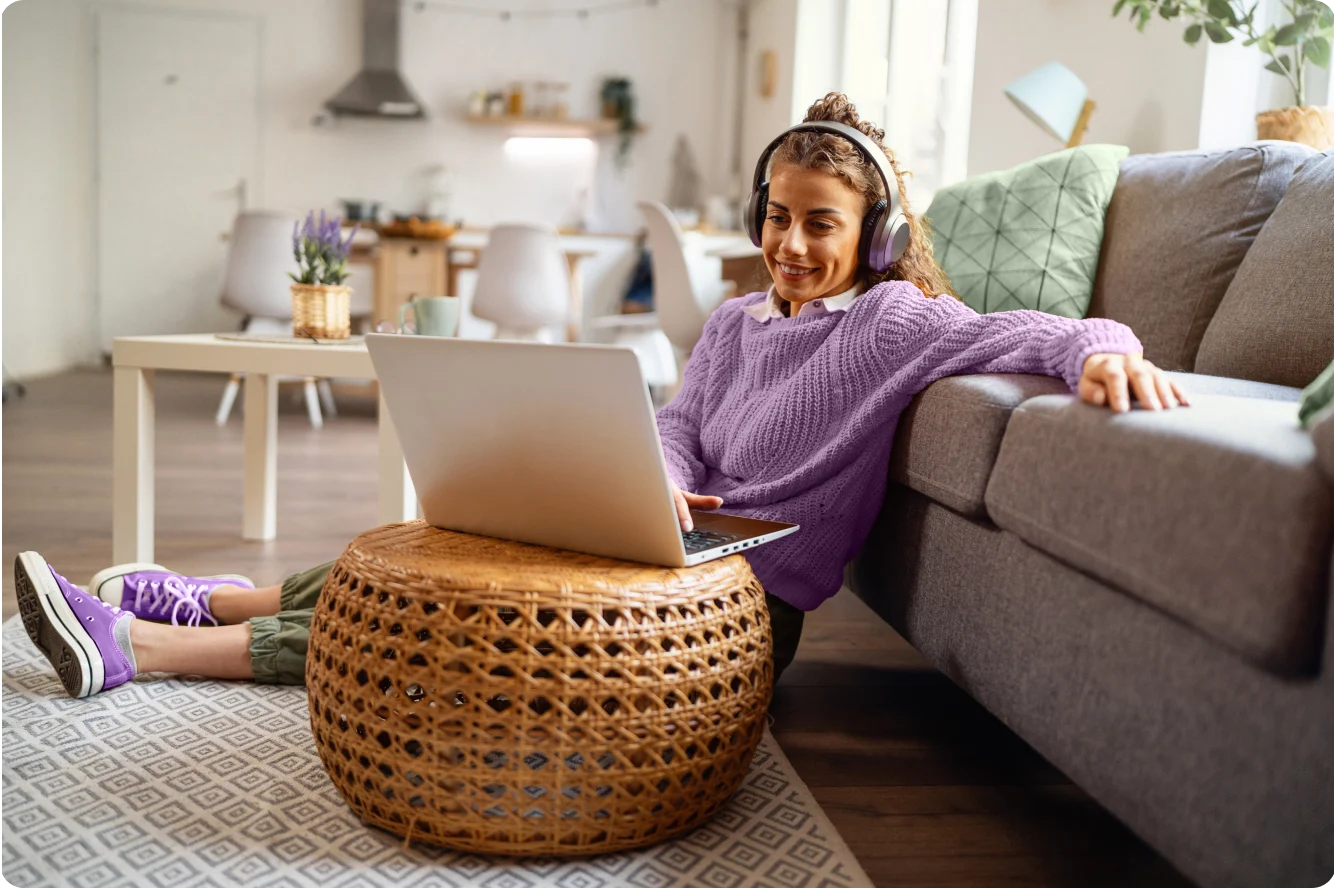 An image of a young woman sitting on the floor of her living room, reading the TELUS SmartEnergy blog on her laptop. She is dressed in relaxed clothing and she has a calm and happy facial expression.