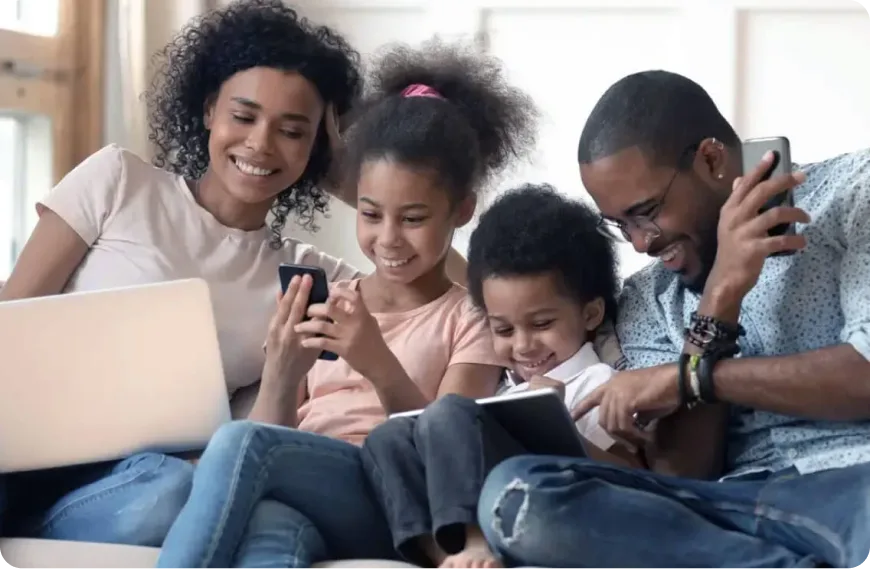 A family sitting together on the couch, laughing and sharing devices connected to TELUS PureFibre.