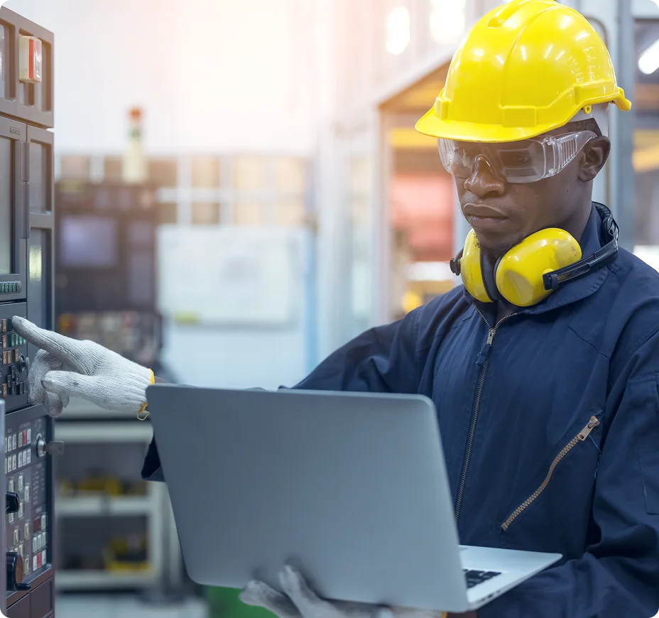 Industrial worker with safety equipment using laptop at construction site.
