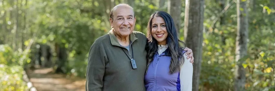 An elderly man and his daughter smile together on a wooded trail. He wears a discreet emergency pendant, demonstrating how medical alert systems for seniors Canada provide peace of mind and safety for active families enjoying the outdoors.