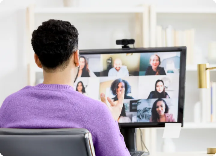 Person in a purple sweater hosts a video meeting on a desktop monitor.