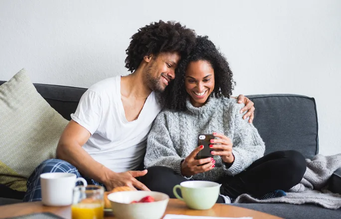 A couple are seen on the couch reviewing cameras on the TELUS SmartHome+ app.