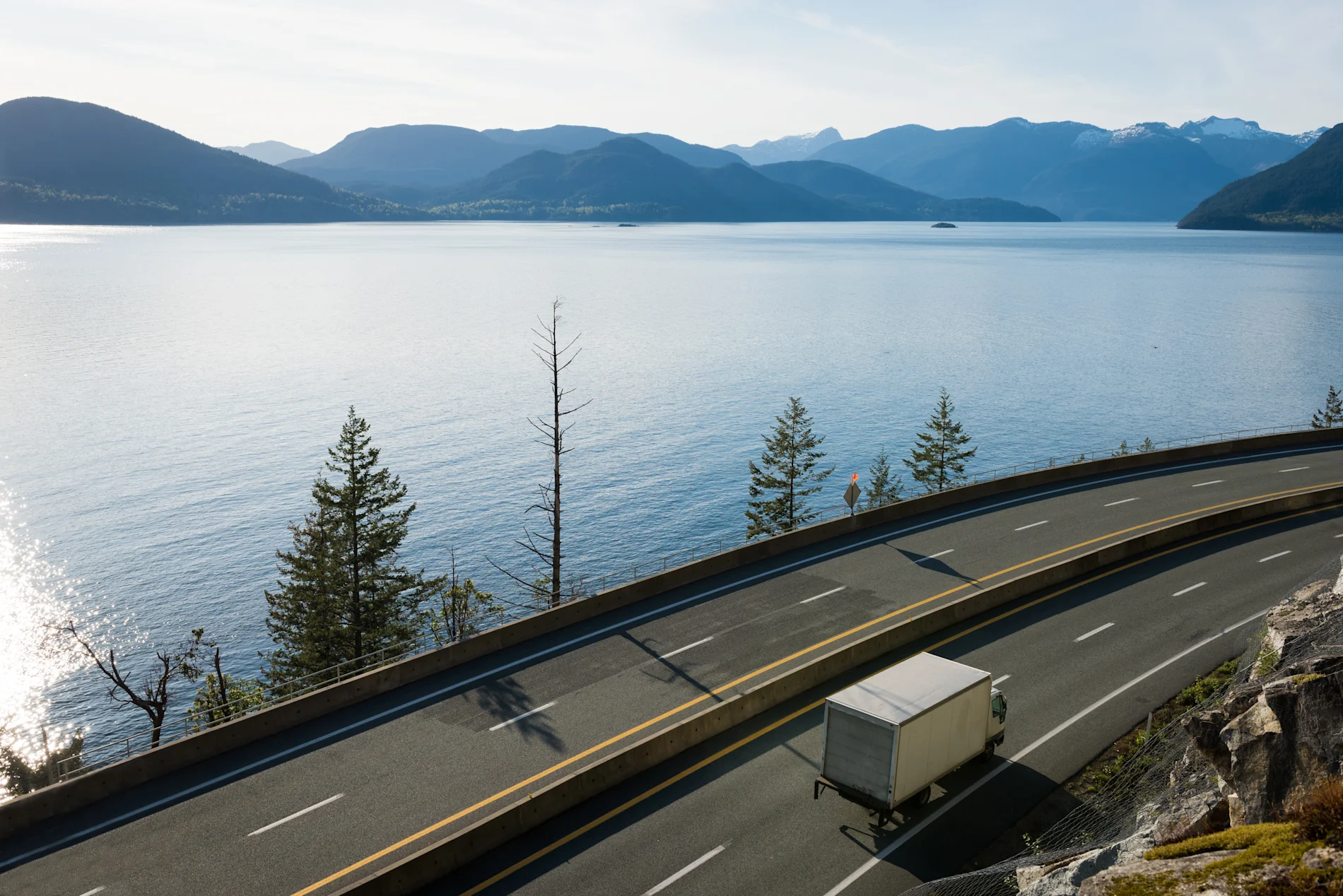 Small transport truck driving down highway in the mountains by a lake