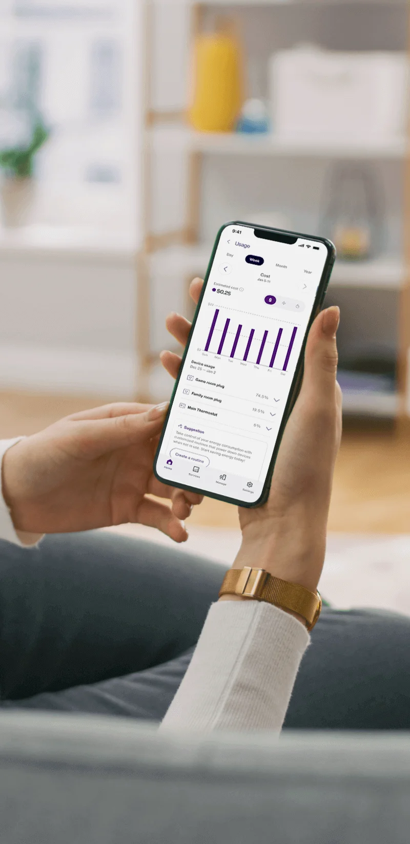 Personne assise sur le sofa du salon et tenant en main un appareil sur lequel l’application TELUS MC+ affiche la consommation d’énergie.