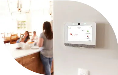 A security panel on a wall in a home with a family in the background.