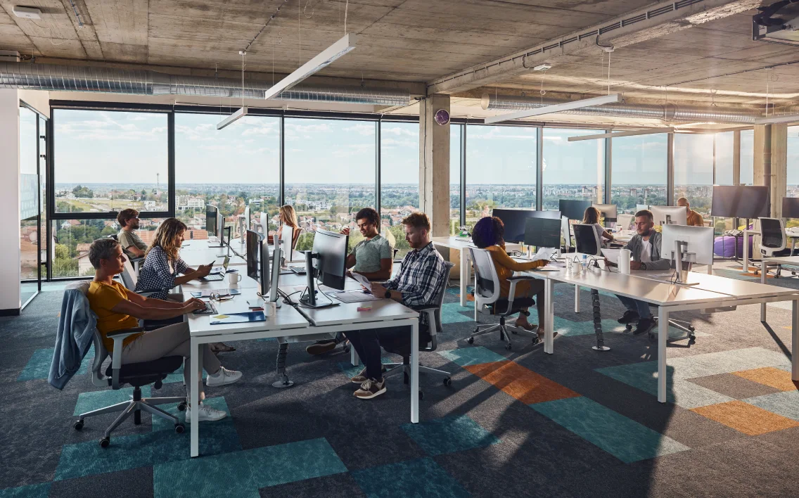 A group of people working in an open space office at different desks.