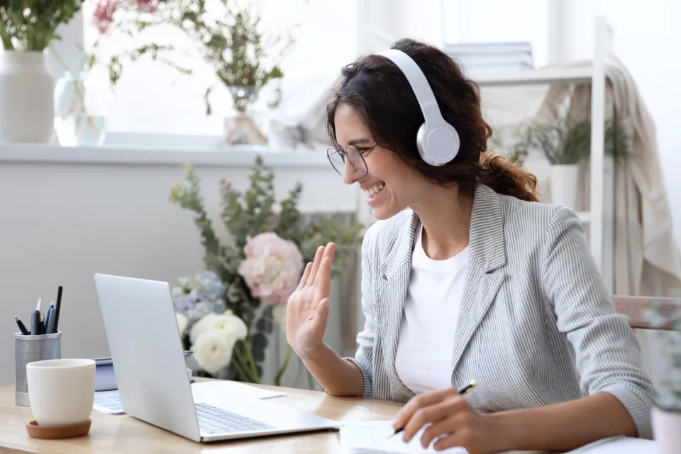 A woman wearing headphones, waving hello to meeting colleagues