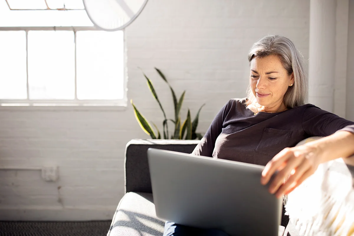 A woman looks at her laptop while sitting on a couch