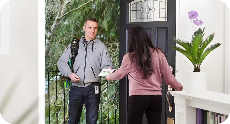 Un électricien certifié TELUS arrive à domicile pour installer et jumeler l'équipement Énergie intelligente, tandis qu'une femme l’accueille à la porte.