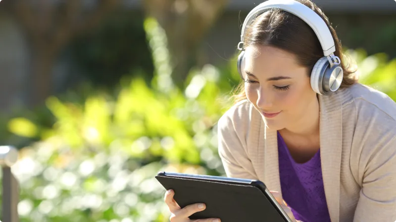 A woman sitting outside and watching a show on her tablet, symbolizing the on-the-go streaming capability of Stream+.