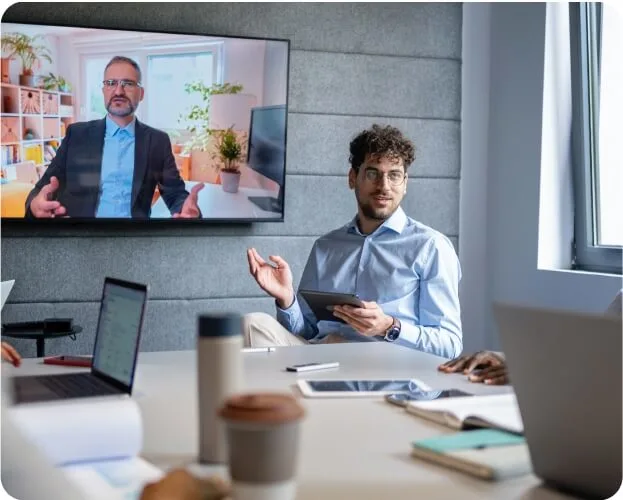 Business professionals gathered in a meeting room with a laptop and a television for a presentation or discussion.
