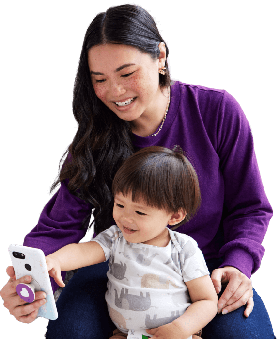Young mom at home with her toddler, engaging with a smartphone.