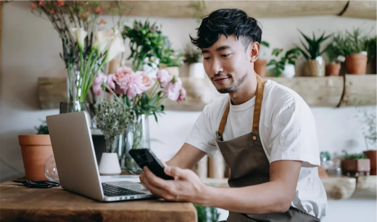 Man sitting at desk in front of a laptop while looking at phone