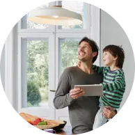 Avec son fils dans les bras, un père contrôle les appareils intelligents de sa maison via l’application Maison connectée+ sur une tablette.