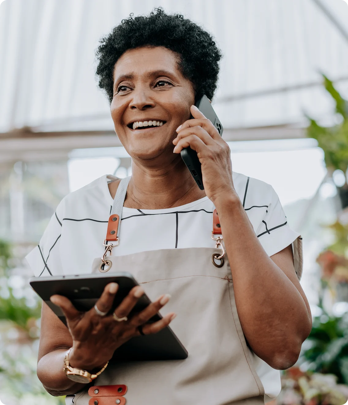 Garden shop owner smiles while on a call and holding a tablet.