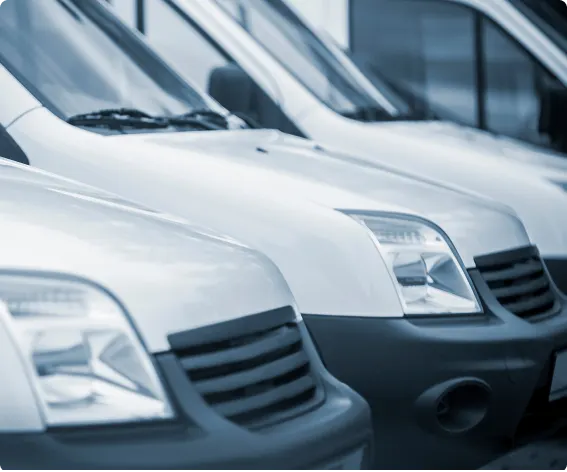 Row of white commercial delivery vans in fleet parking lot.