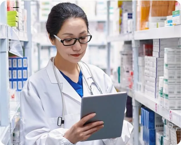 A female pharmacist in a pharmacy, focused on using a tablet to manage prescriptions and patient information.