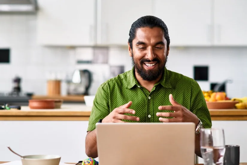 Un homme assis dans sa cuisine utilise son ordinateur portable pour faire un rendez-vous virtuel avec son coach en santé.