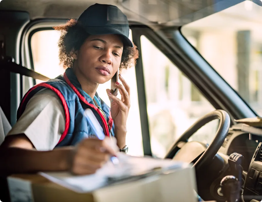 A fleet driver talks on the phone while filling out paperwork in a van