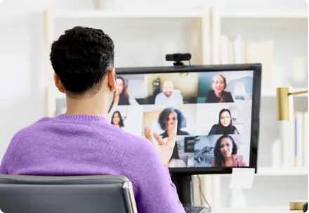 Person in a purple sweater hosts a video meeting on a desktop monitor.