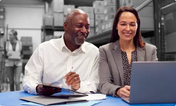 Two colleagues sitting at a desk and viewing a laptop.