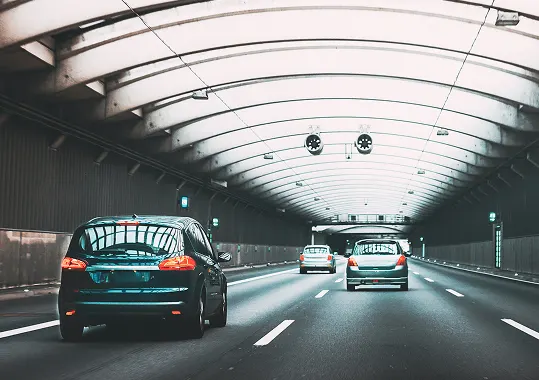 Commercial vehicles driving through illuminated tunnel.