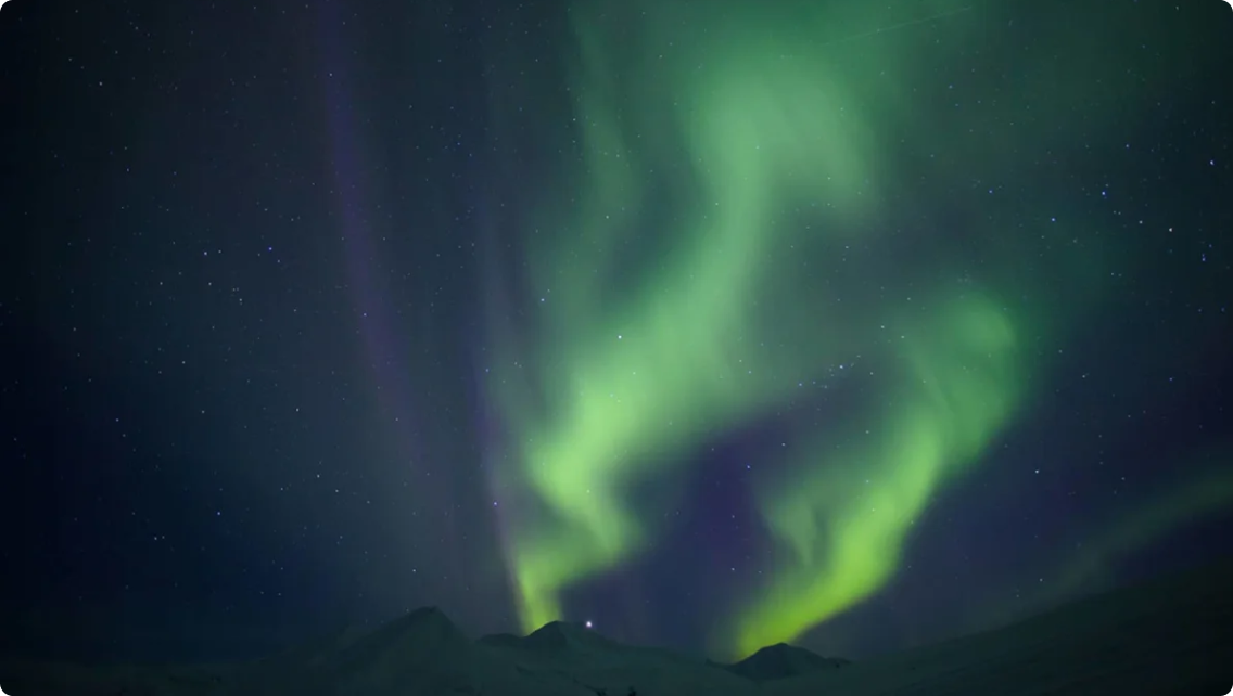 The Northern Lights (Aurora Borealis) shining from behind a ridge of mountains.