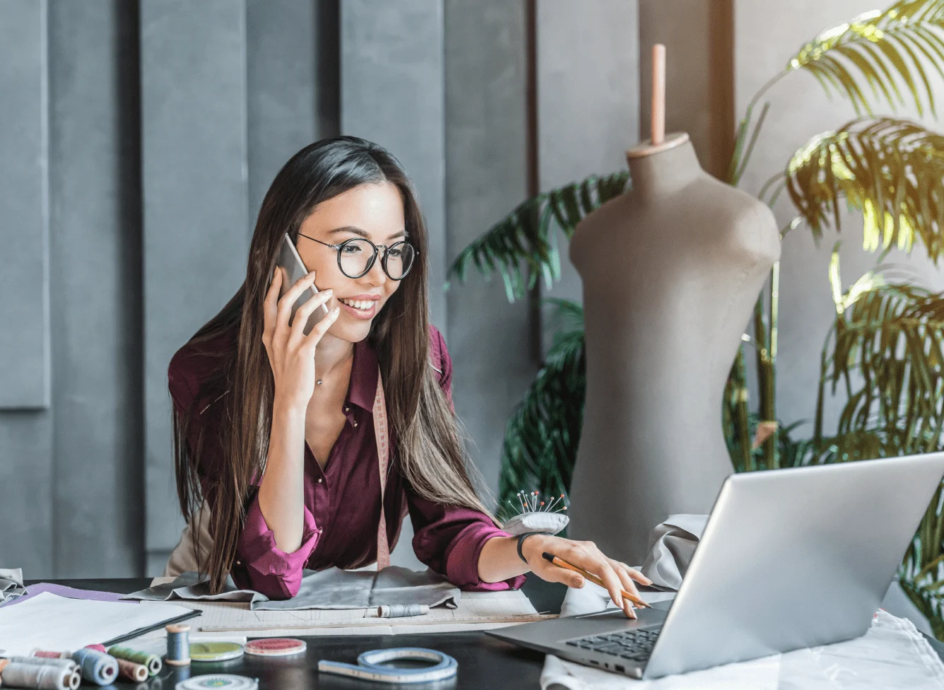 Une designer de mode est au téléphone tout en travaillant sur son ordinateur portable.